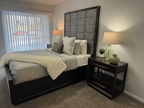 A bedroom with a large bed and a nightstand with a lamp. at The Park on 13 Apartments - Royal Oak, MI Apartments, Michigan, 48073