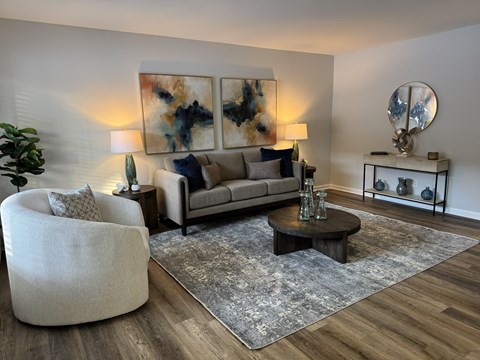 A modern living room with a grey sofa, a round chair, a coffee table, and a large abstract painting on the wall.