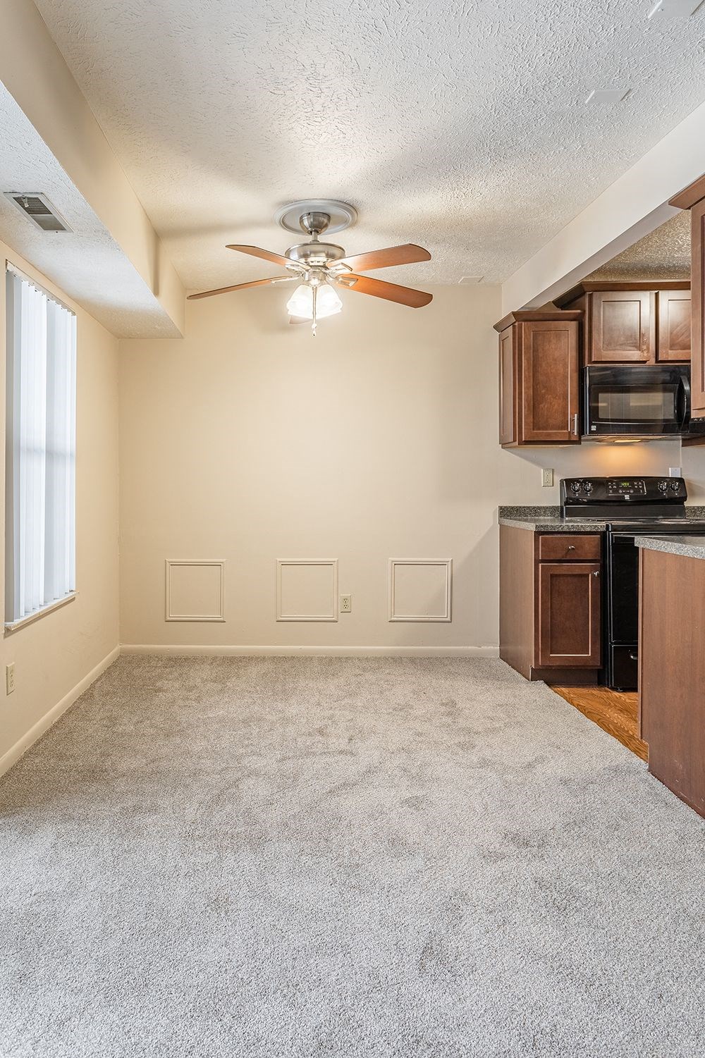 an empty living room with a ceiling fan and a kitchen