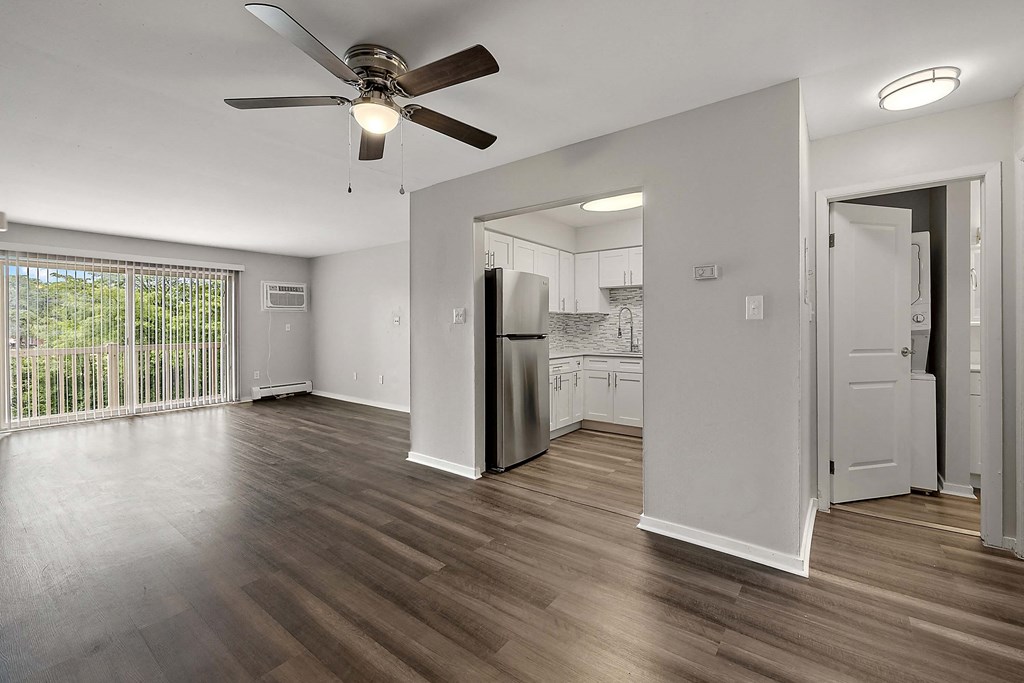 an empty living room with a refrigerator and a ceiling fan