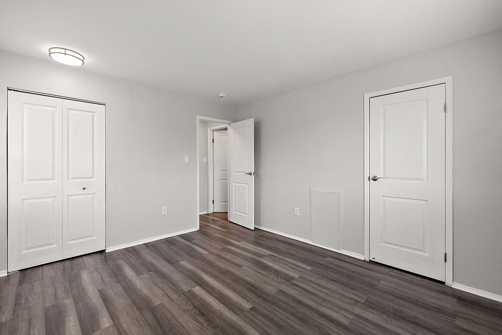 an empty living room with white doors and wood flooring