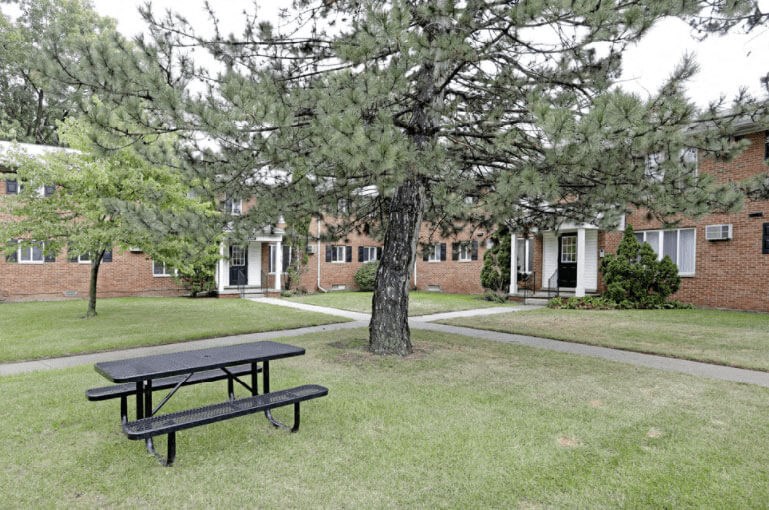 A black picnic table is in the foreground of a grassy area in front of a brick building.