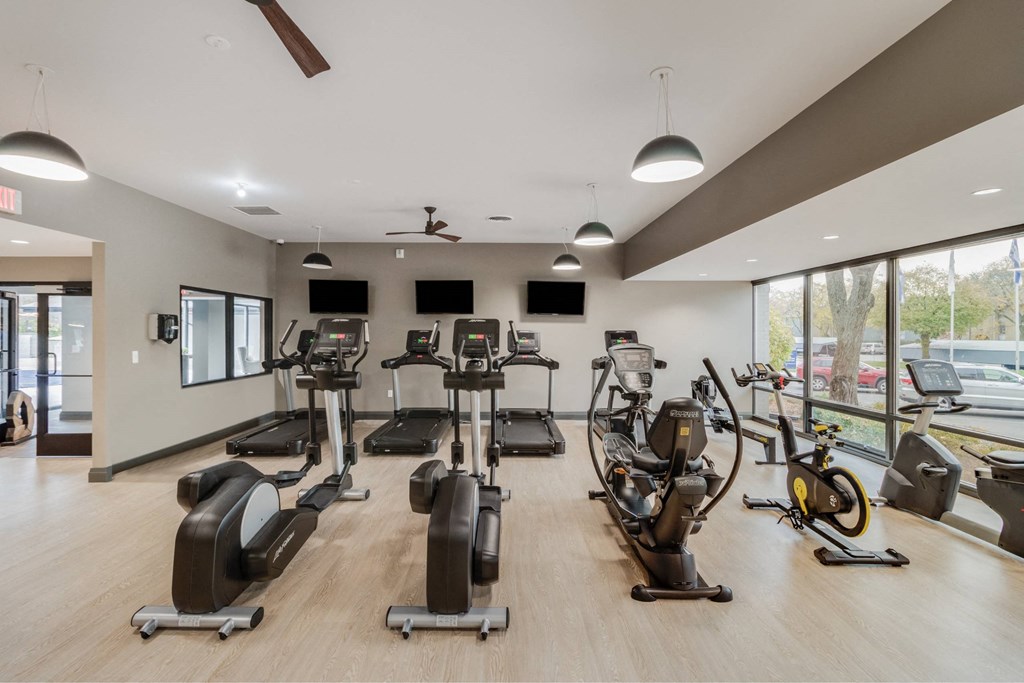 A gym with a variety of exercise equipment including treadmills, stationary bikes, and elliptical machines at The Waverly on the Lake - Belleville, MI Apartment, Belleville, MI, 48111