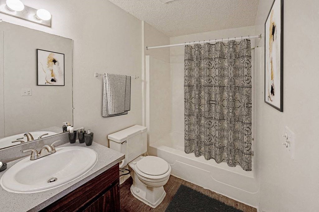 A bathroom with a toilet, sink, and shower curtain at The Waverly on the Lake - Belleville, MI Apartment , Belleville