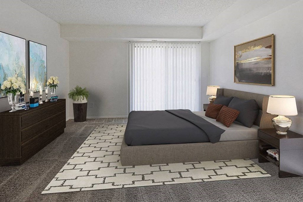 A bedroom with a large bed, a nightstand with a lamp, and a painting on the wall at The Waverly on the Lake - Belleville, MI Apartment , Belleville, 95050