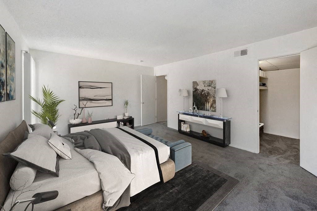 A bedroom with a bed, nightstand, and a plant at The Waverly on the Lake - Belleville, MI Apartment , Belleville, Michigan