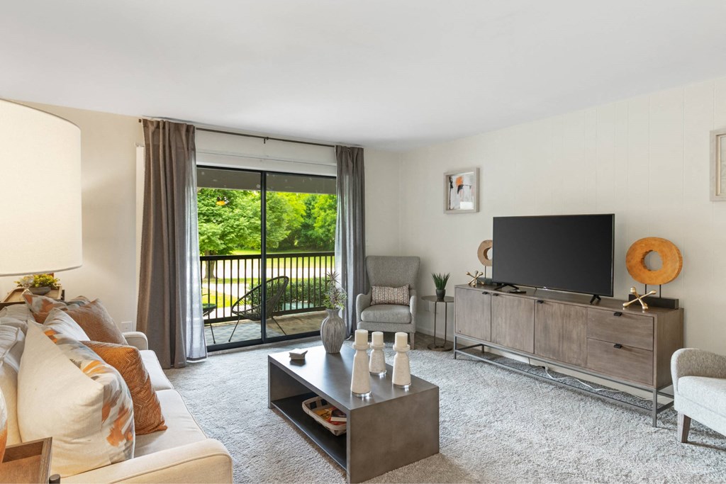 A living room with a white couch, a coffee table, a television, and a sliding glass door at The Waverly on the Lake - Belleville, MI Apartment , Belleville