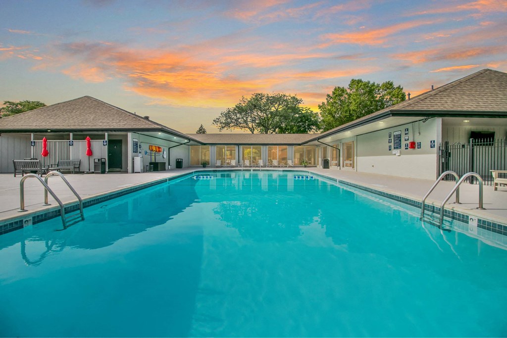 A large swimming pool in front of a building with a sunset in the background at The Waverly on the Lake - Belleville, MI Apartment , Belleville, MI