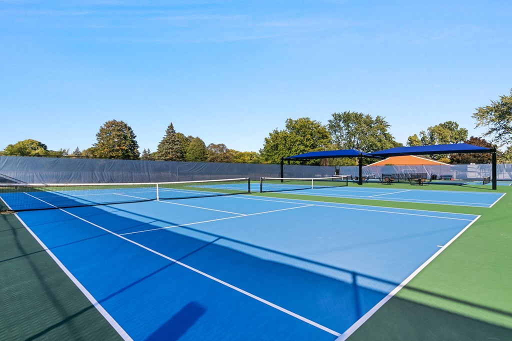 A tennis court with a blue surface and white lines at The Waverly on the Lake - Belleville, MI Apartment , Michigan, 95050