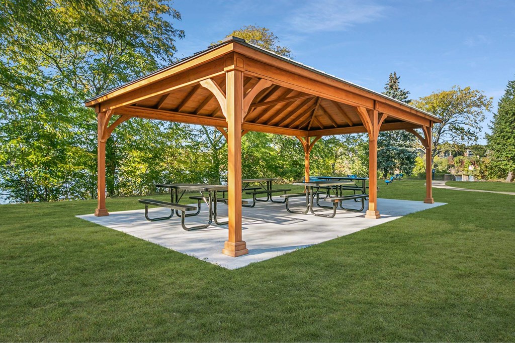 A wooden pavilion with a white base and a roof is surrounded by a grassy area at The Waverly on the Lake - Belleville, MI Apartment, Belleville, MI, 95050