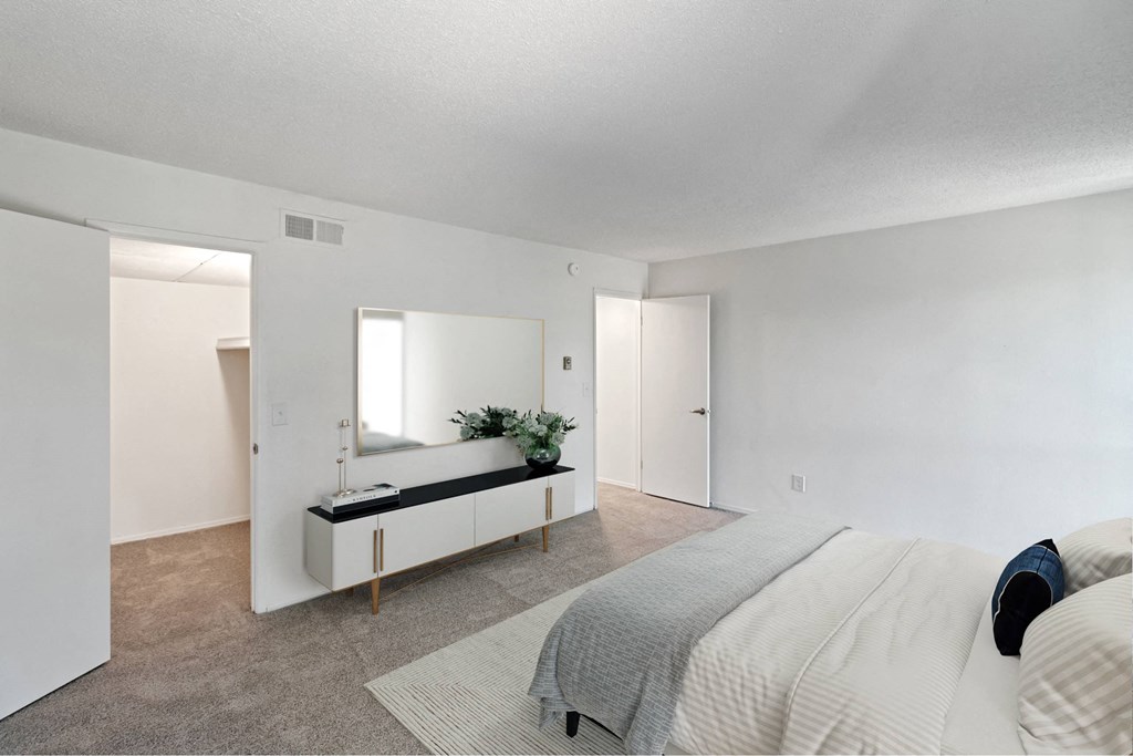 A bedroom with a bed, a mirror, and a bench with a plant on it at The Waverly on the Lake - Belleville, MI Apartment, Belleville, MI, 95050