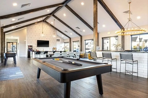 A pool table is in the middle of a room with a bar and chairs.