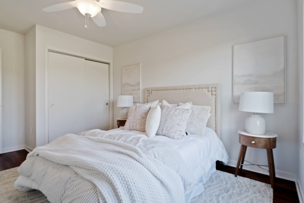 A bedroom with a bed, pillows, a ceiling fan, and a lamp.