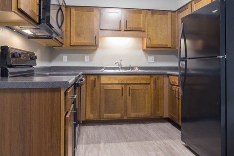 A kitchen with wooden cabinets and a black refrigerator.