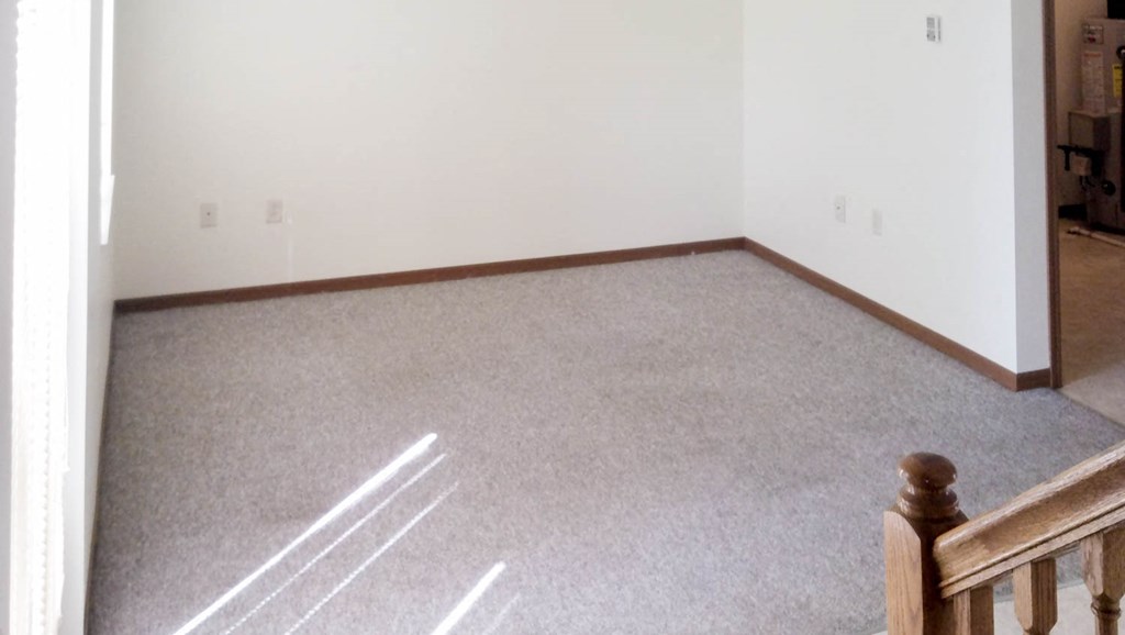 A room with a carpeted floor and a wooden staircase.