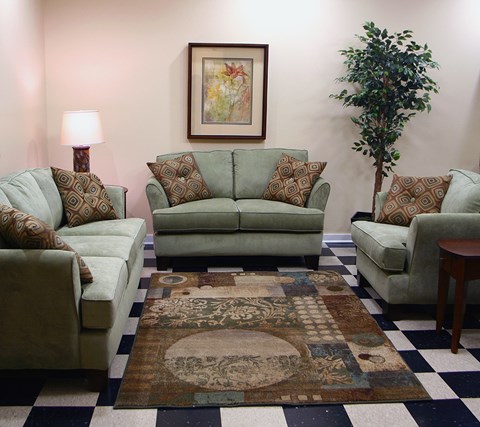 A living room with a green couch, a brown and white rug, and a green armchair.