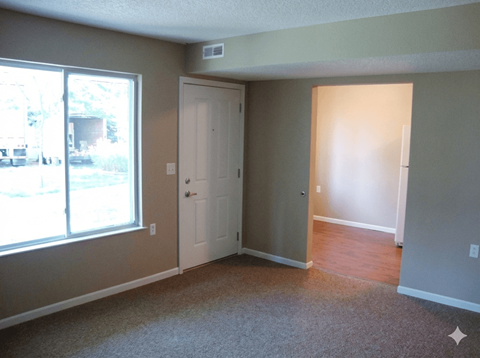 A room with a carpeted floor, a door, and a window.