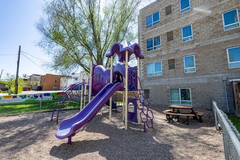 A purple slide in a playground with a building in the background.