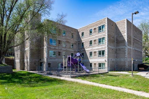 A playground with purple slides is in front of a brick building.