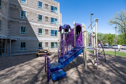 A playground with purple and blue slides in front of a building.