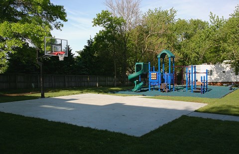 A basketball court with a basketball hoop and a playground with slides in the background.