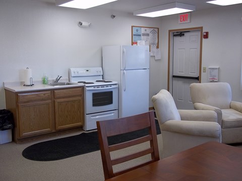 A kitchen with a refrigerator, oven, and a table with a chair.