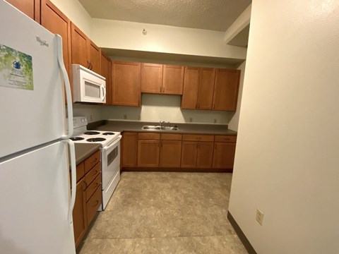 A kitchen with a white fridge, white microwave, and brown cabinets.