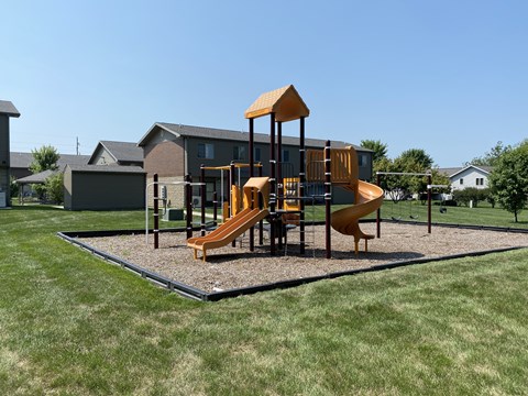 A playground with a yellow slide and a brown structure.