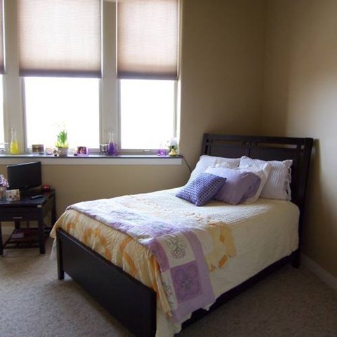 A bedroom with a bed, a desk, and a window.