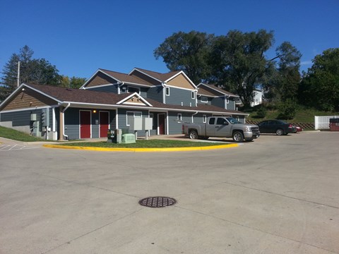 A building with a grey roof and a red door is surrounded by a parking lot.