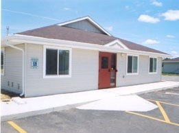 A small building with a red door and a parking lot in front.