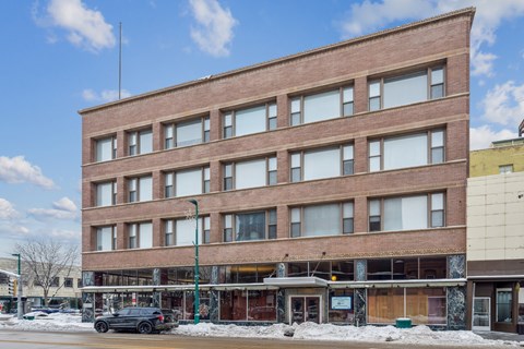 A large brown building with many windows sits on a street corner.