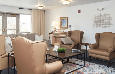 A living room with a brown chair in the foreground and a white wall with a picture frame and a fire alarm.