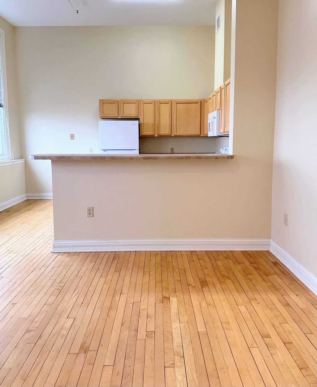 an empty living room with wood floors and a kitchen