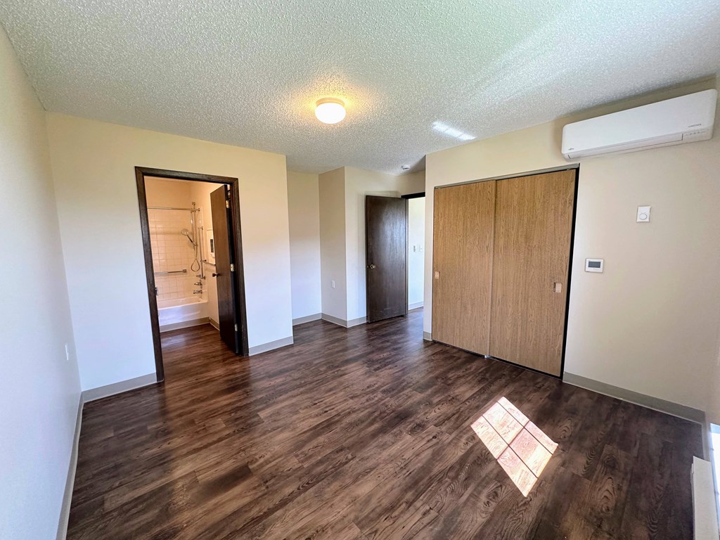 an empty living room with wood flooring and a door to a bathroom