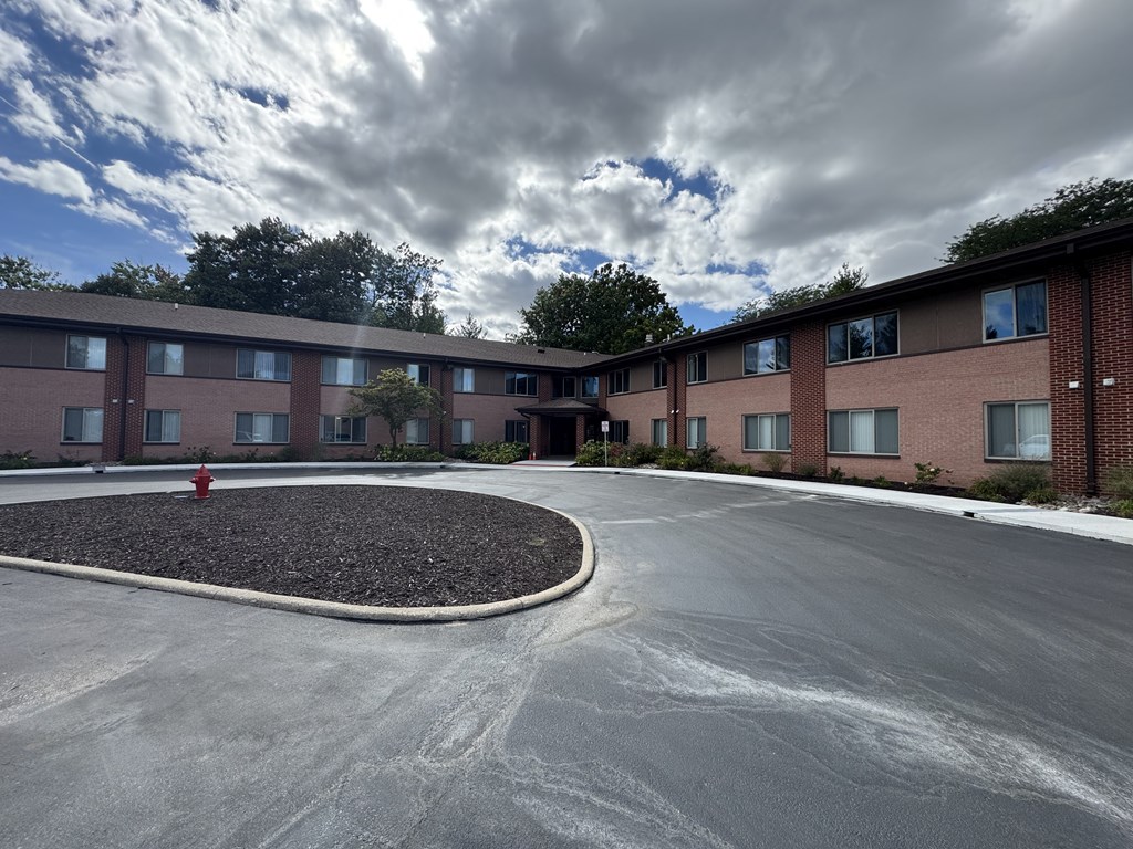 A red fire hydrant sits in the middle of a gravel circle in front of a building.