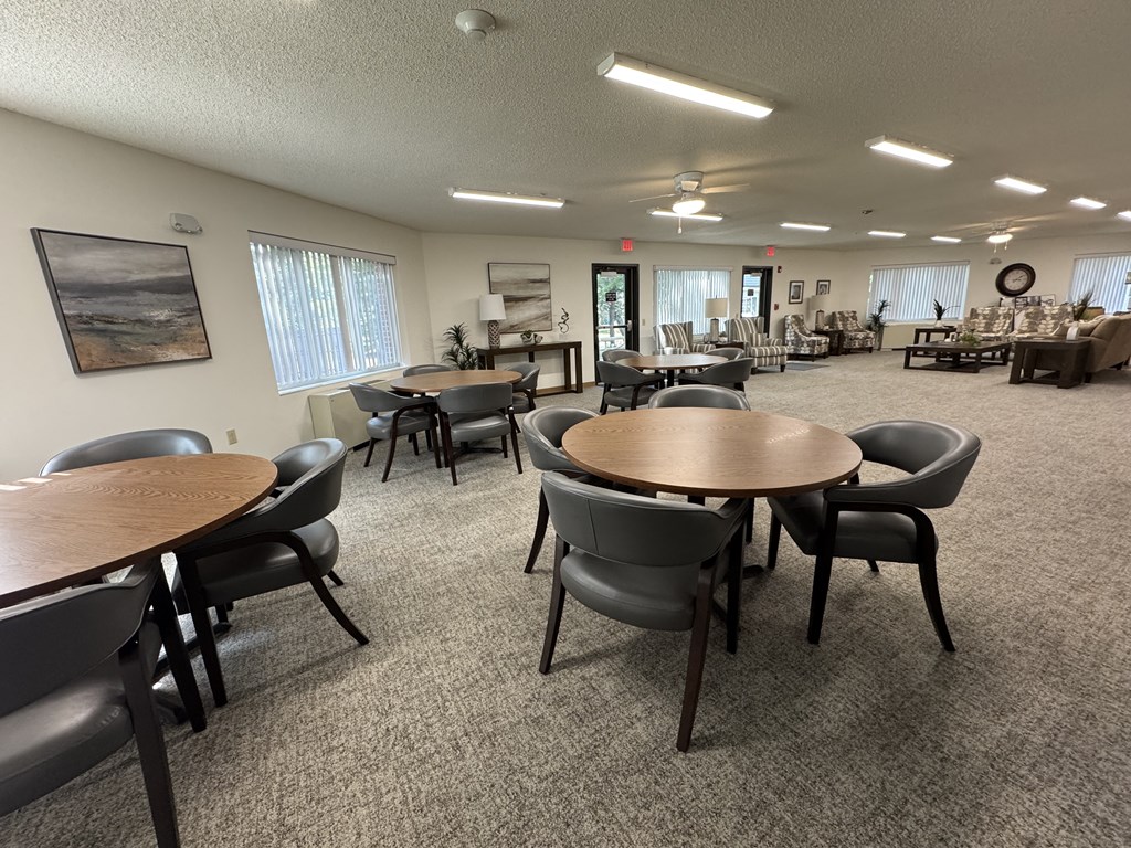 A room with a carpeted floor and a large table surrounded by chairs.