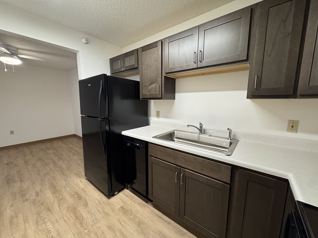A kitchen with a black refrigerator and brown cabinets.