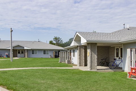A grassy area in front of a building with a bicycle leaning against the wall.
