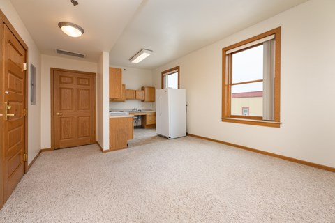 A kitchen area with a refrigerator, cabinets, and a window.