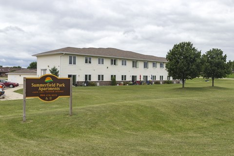 A sign for Summerfield Park Apartments stands in front of a white building.