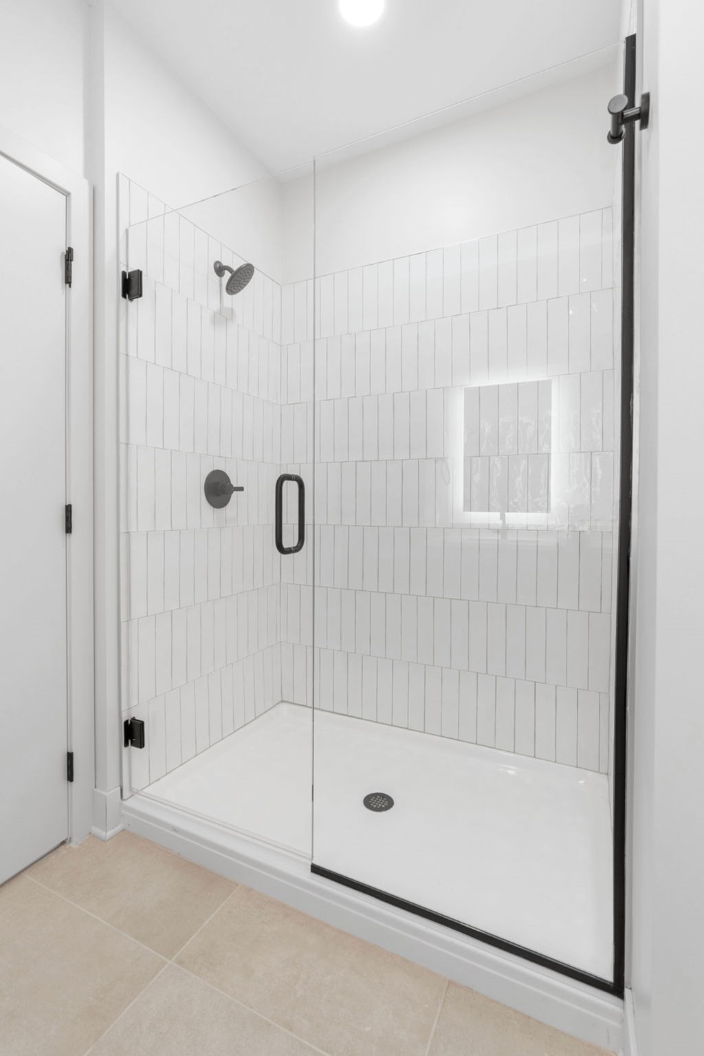 A white tiled shower with a black handle and a black door.