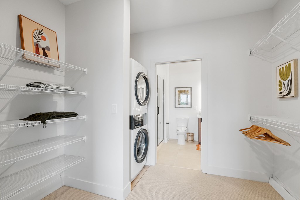 A walk-through closet attached to the bedroom, leading to the bathroom in a one-bedroom, one-bathroom apartment home at Lilia in Lilydale, MN 55118. Features in-unit laundry and storage.