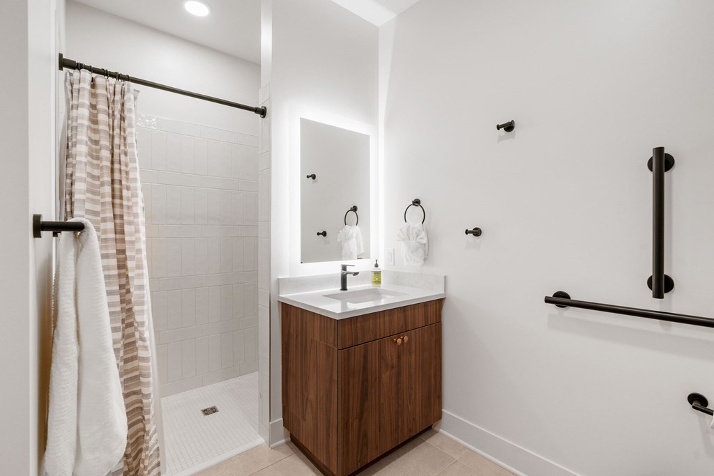A bathroom with a vanity, backlit mirror, toilet, and walk-in shower in the Guest Suite, a reservable community amenity at Lilia in Lilydale, MN 55118