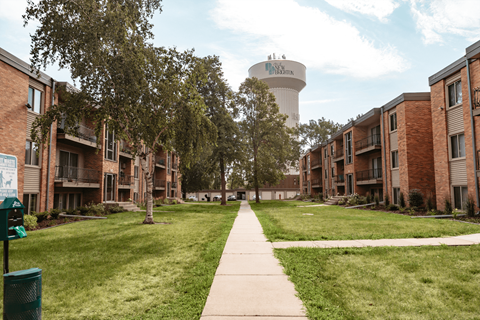 A long concrete walkway leads through a grassy area between two rows of apartment buildings.