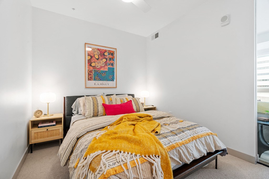 A bedroom with a bed, a nightstand with a lamp, and a framed picture on the wall. at The Mera, Minnesota, 55426