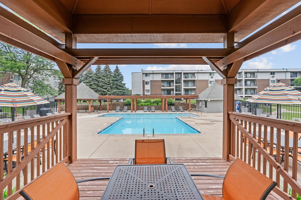A wooden deck with a table and chairs overlooking a pool.