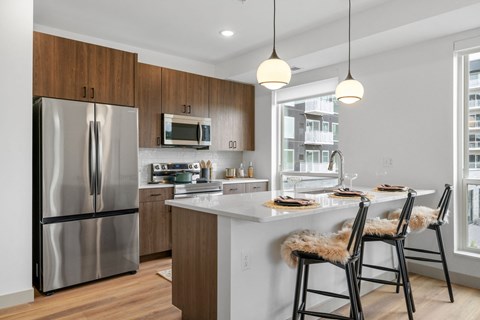 a kitchen with a large island with stools and a stainless steel refrigerator