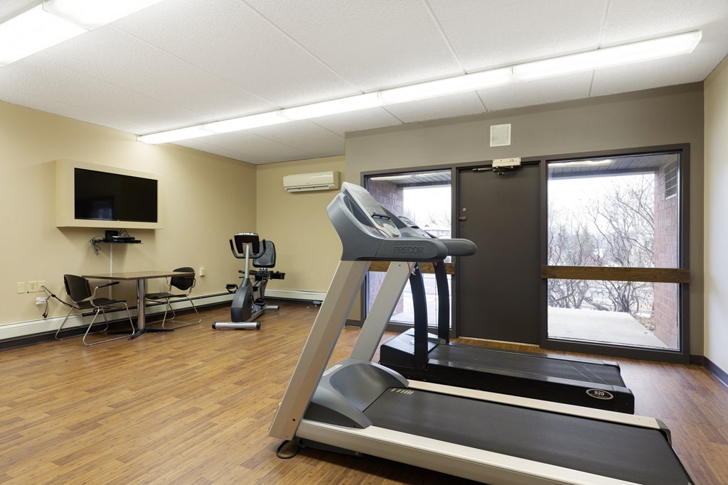 A treadmill is in the middle of a room with a television and exercise equipment.