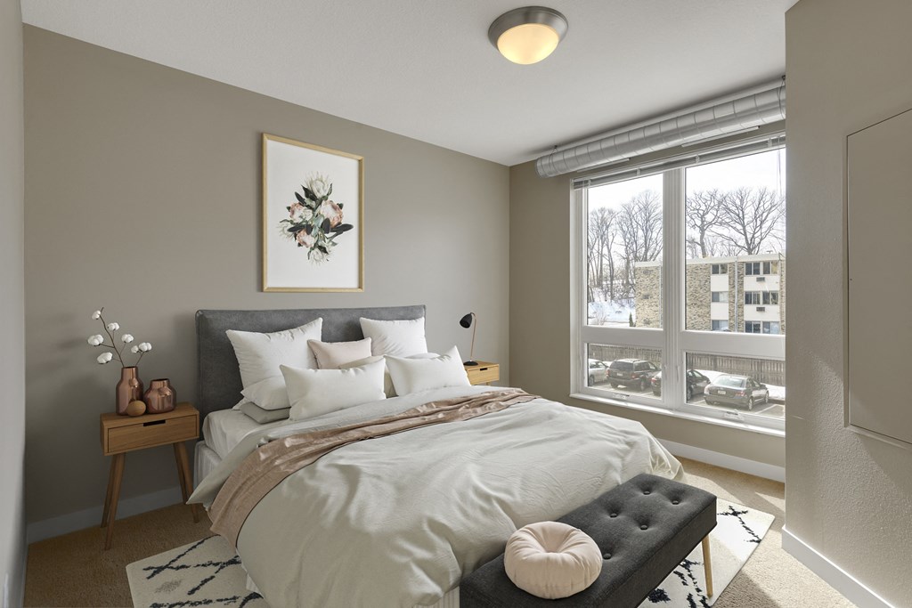 a bedroom with a large window and a bed with a white comforter and pillows at Be @ Axon Green, Minneapolis, 55416